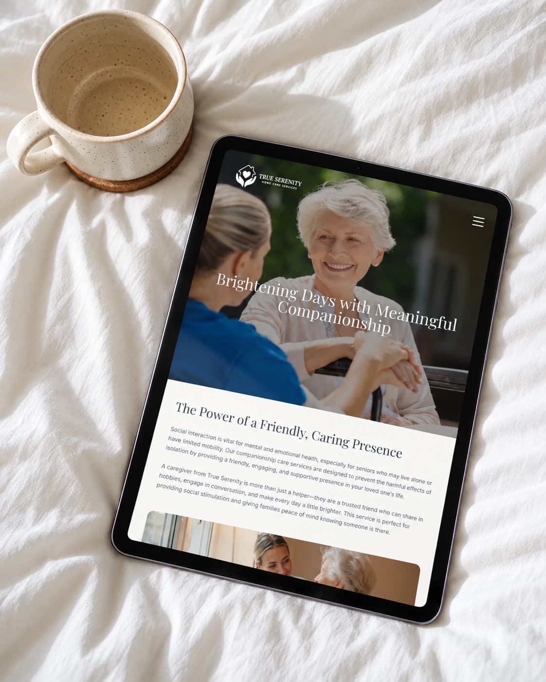 True Serenity companionship care service page on a tablet, on bed linen beside a mug