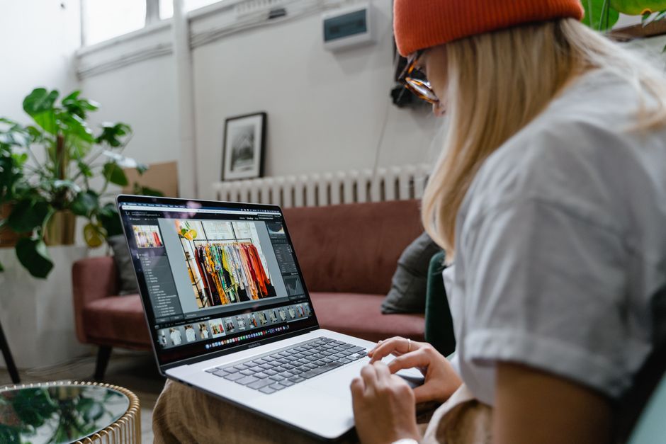Woman using a laptop for photo editing in a cozy, plant-filled living room setting.